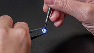 iD100 Photoshoot Close up of hands holding a loose stone with tweezers in one hand, and using the iD100 probe to highlight the stone in the other on a black background.