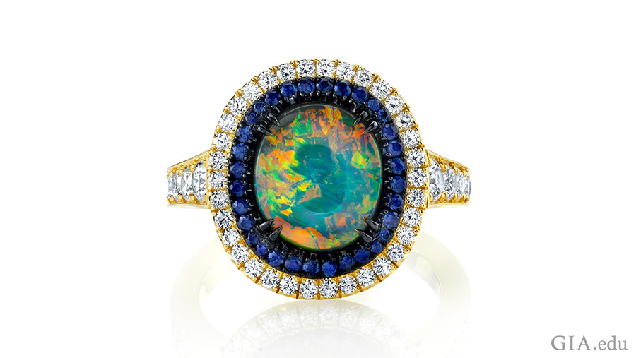 Sapphires and diamonds encircle the October birthstone, a 1.92 carat black opal in a stunning 18K yellow gold and black rhodium ring. Sapphires and diamonds encircle the October birthstone, a 1.92 carat black opal in a stunning 18K yellow gold and black rhodium ring.